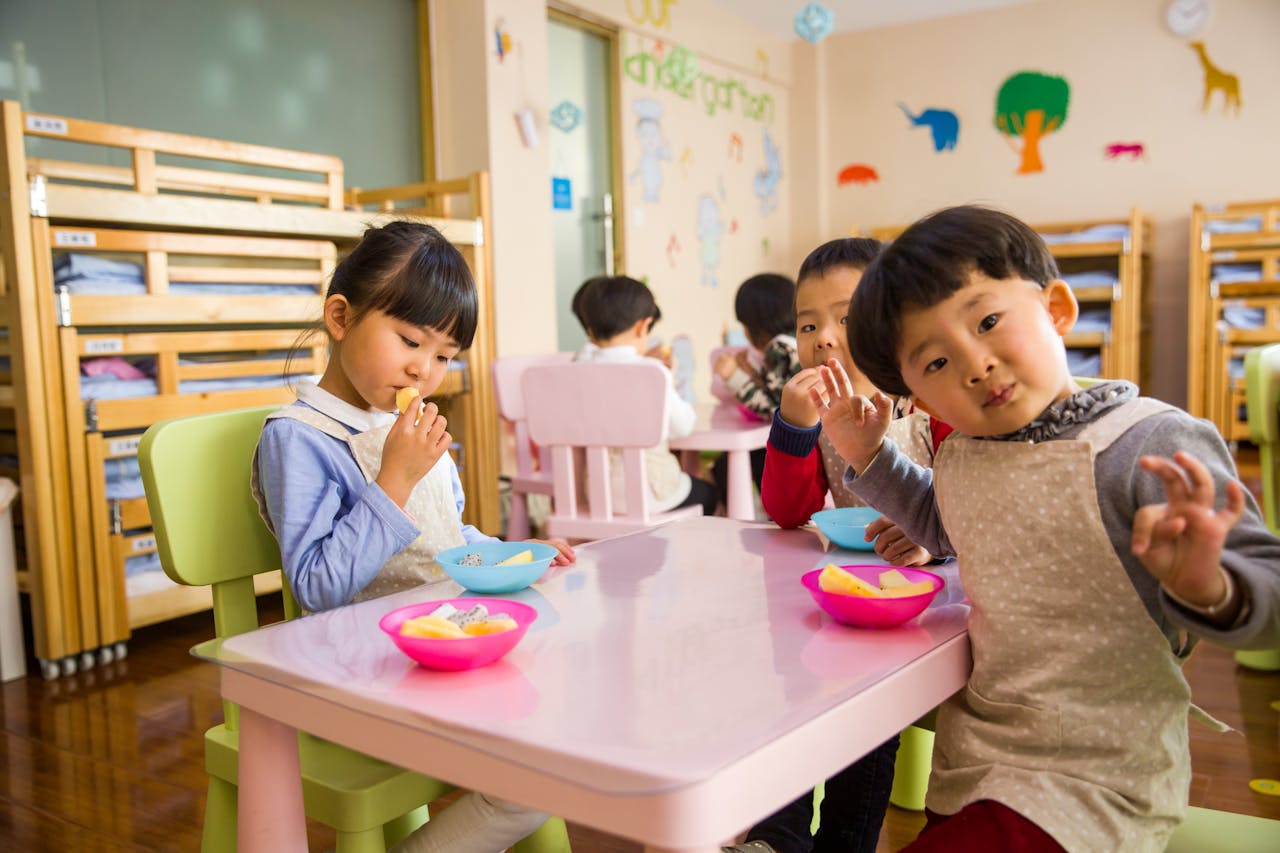 creative Kids seated around a table in a colorful classroom, eating snacks happily.