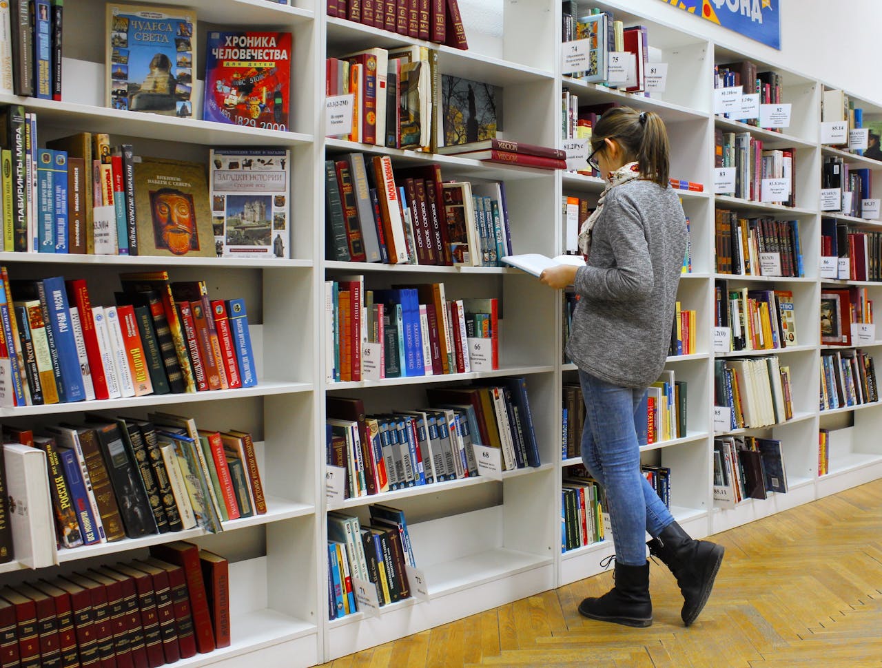 why-choose-us A young woman stands reading a book in a well-stocked library.