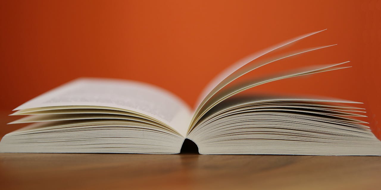 mobile-02 An open book with pages turning against a vibrant orange background, symbolizing knowledge and education.