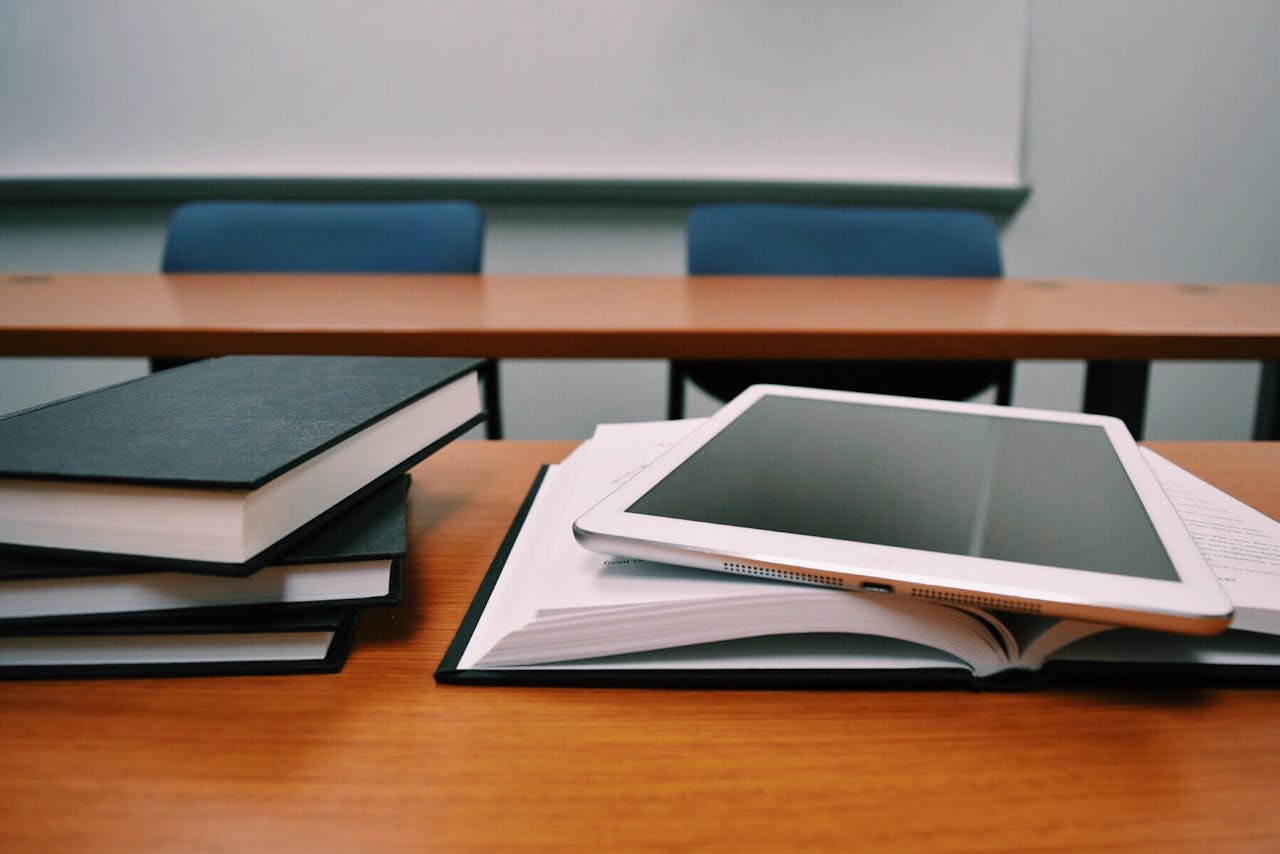 Services-01 Books and a tablet on a desk in a classroom, depicting modern education.